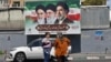 Women stand on a street in Tehran in front of a billboard with portraits of the three men who have been supreme leaders of the Islamic republic: Ayatollah Ruhollah Khomeini (left), Ayatollah Ali Khamenei (center), and the incumbent, Mojtaba Khamenei. 