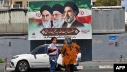 Women stand on a street in Tehran in front of a billboard with portraits of the three men who have been supreme leaders of the Islamic republic: Ayatollah Ruhollah Khomeini (left), Ayatollah Ali Khamenei (center), and the incumbent, Mojtaba Khamenei. 