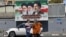 Women stand on a street in Tehran in front of a billboard with portraits of the three men who have been supreme leaders of the Islamic republic: Ayatollah Ruhollah Khomeini (left), Ayatollah Ali Khamenei (center), and the incumbent, Mojtaba Khamenei. 