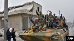 Syrian pro-government forces sit on a military vehicle driving past residents fleeing the eastern part of Aleppo on November 30.