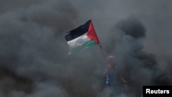 Dječak drži palestinsku zastavu dok stoji usred dima uoči 70. godišnjice Nakbe, na granici Izraela i Gaze istočno od grada Gaze 14. maja 2018. 