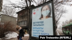 Қала әкімдігінің маска тағуға шақырған постерінің жанынан өтіп бара жатқан қыз. Алматы 13 желтоқсан 2020 жыл.