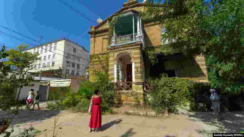 Девушка фотографирует на смартфон старинный дом из ракушечника на улице Дувановской