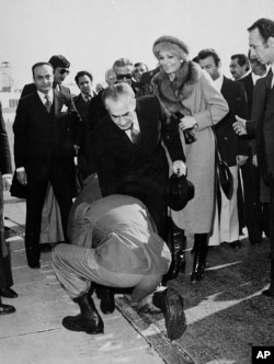 In this Jan. 16, 1979 file photo, a soldier bends to kiss the feet of Iran's Shah Mohammad Reza Pahlavi on the tarmac of Mehrabad Airport in Tehran, Iran. Behind the shah is his wife, Empress Farah.