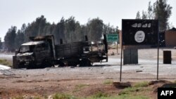 Разрушенный автомобиль на фоне билборда ИГ в сирийской селе близ Ракки. 