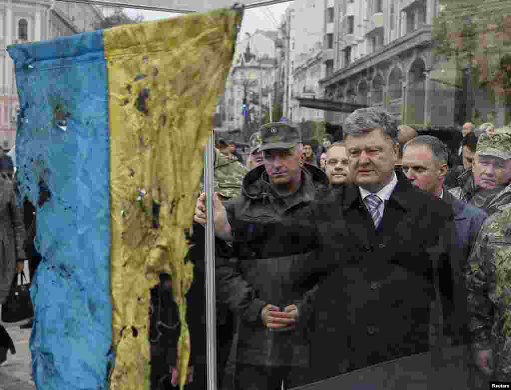 Ukrainian President Petro Poroshenko (center) looks at a Ukrainian flag retrieved from the bloody retreat from Ilovaisk in eastern Ukraine in late August 2014. The country marks Defenders Day on October 14. (Reuters/Gleb Garanich)