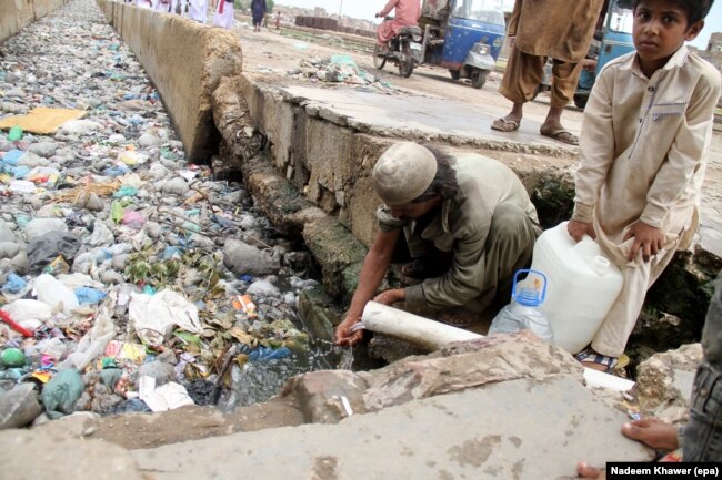 Люди набирают воду для питья и домашних надобностей прямо из свинцовой трубы, выходящей в сточную канаву. Хайдарабад, Пакистан, 2019 год