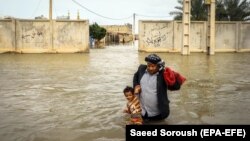 An Iranian man carries his son in a flooded way in a village around the city of Ahvaz, Khuzestan province, March 31, 2019