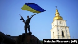 A woman waves a Ukrainian flag atop a destroyed Russian tank on display at an open-air exhibition of destroyed military equipment of Russian Army in Kyiv.