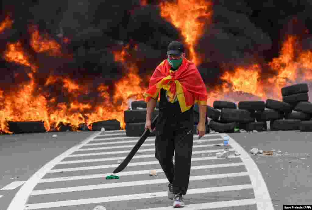 Мужчина проходит мимо горящих покрышек у баррикады, созданной, чтобы заблокировать доступ к историческому городу Цетине во время акции протеста против инаугурации нового главы Сербской православной церкви