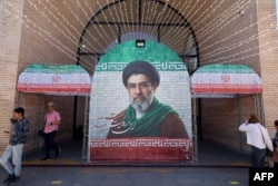 Commuters walk past a tiled image of current leader Ayatollah Mojtaba Khamenei near a Tehran subway station on May 9.