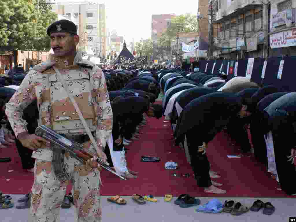 A Pakistani security officer guards praying Shi'a during Ashura ceremonies in Hyderabad.