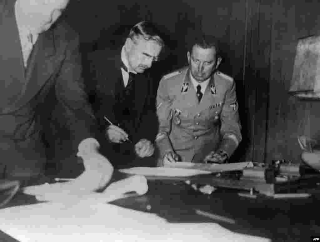 U.K. Prime Minister Arthur Neville Chamberlain (left) signs the Munich Agreement as Hitler's secretary, Martin Bormann, looks on in Munich in the early hours of September 30, 1938 (although the document was dated September 29).