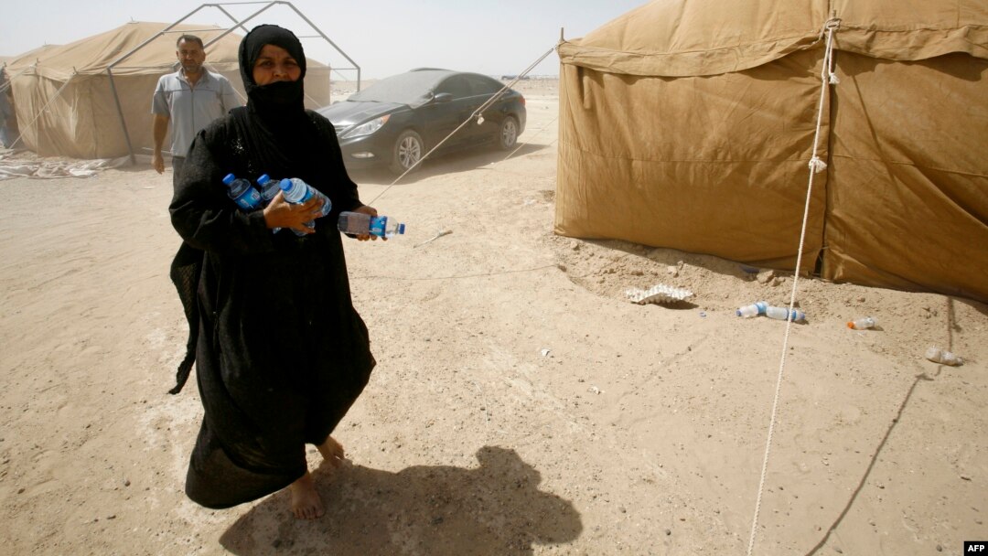 A displaced Iraqi woman who fled Anbar Province due to the ongoing conflict between pro-government forces and Islamic State militants carries bottles of water at a makeshift camp for internally displaced persons some 30 kilometers south of Fallujah on May 25.