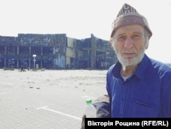 85-річний мешканець Маріуполя Сергій на тлі розбомбленого ТЦ «Порт Сіті» в Маріуполі. Чоловікові дивом вдалося вибратися з квартири, в яку влучив снаряд. Квітень 2022 року