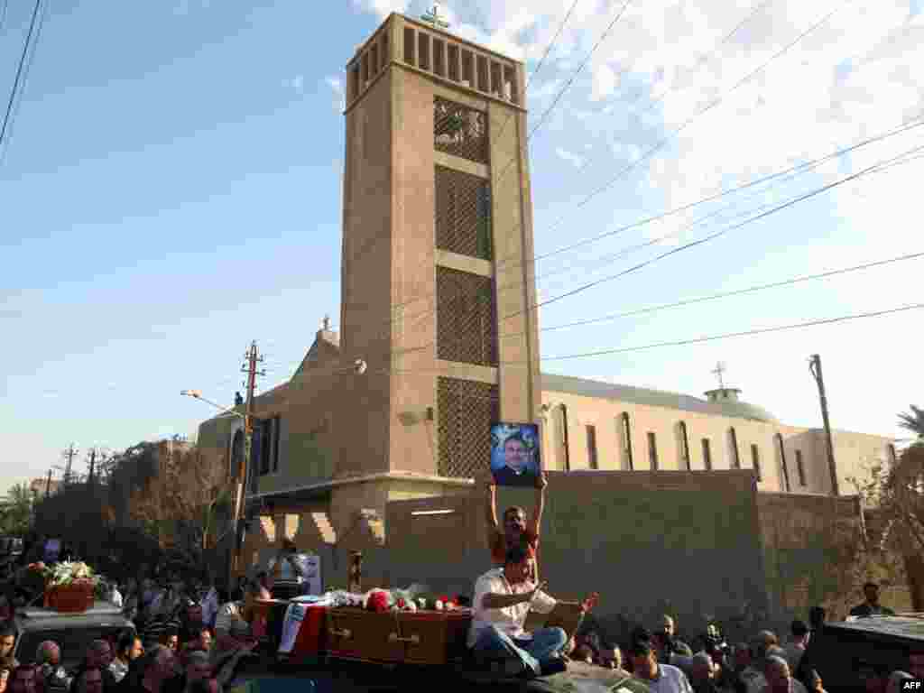 تصویر کشیش ۳۲ ساله‌ای که در جریان گروگانگیری کلیسا بغداد کشته شد در دست عزاداران در بغداد- ۱۱ آبان - IRAQ, Baghdad : Iraqi mourner holds up a portrait of 32-year-old slain priest Taher Saadallah Boutros, known as Father Athir (R), during a funeral procession in Baghdad on November 2, 2010 for the victims of the Syrian Catholic cathedral carnage in which more than 40 Christians, including two priests, were killed on October 31 during a hostage drama with Al-Qaeda gunmen. AFP PHOTO/AHMAD AL-RUBAYE 