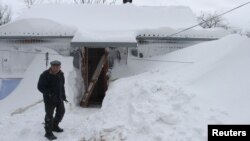 Мужчина стоит у своего дома, заваленного снегом. Иллюстративное фото. 