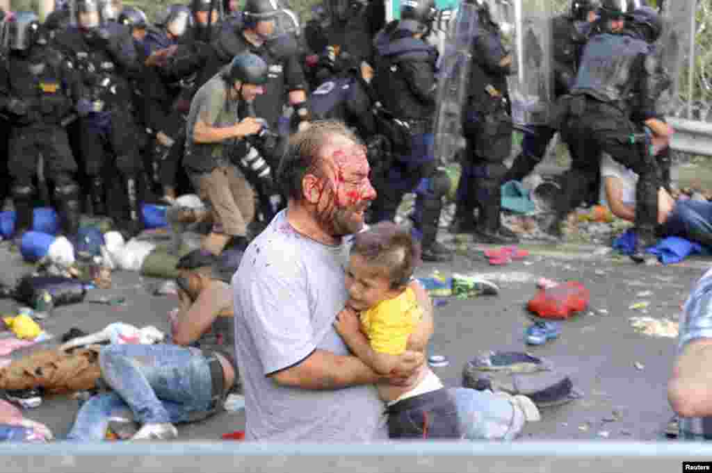 Беженец, пострадавший в столкновениях с венгерской полицией, с ребенком на руках. 16 сентября 2015 года.