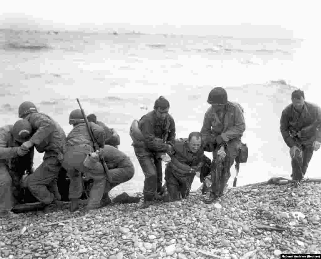 Члены американской десантной группы помогают военным, десантный корабль которых потоплен вражеским огнем у берегов Омахи, недалеко от Коллевиль-сюр-Мер, 6 июня 1944 г.