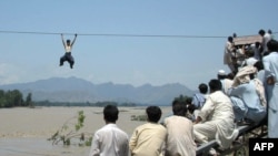 Onlookers perched on a damaged bridge watch a Pakistani flood survivor climb a rope to cross a river in Pakistan's Swat Valley on August 3.