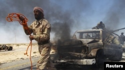 A rebel fighter prepares to tow away a government vehicle mounted with a heavy machine gun after it was hit by a NATO air strike on the eastern outskirts of Brega.