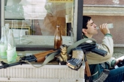 A Bosnian fighter sips a drink next to his Kalashnikov and a statuette of Marshal Tito, the former leader of Yugoslavia, in the Bosnian capital, Sarajevo, in 1992.