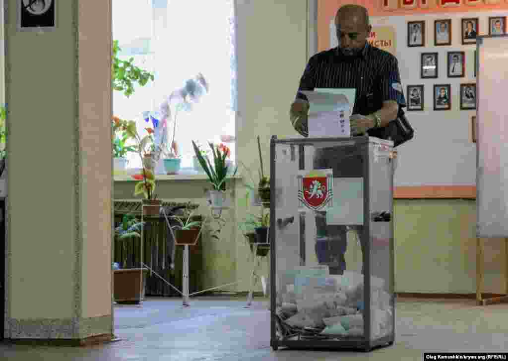 Мужчина кидает заполненные бюллетени в урну для голосования&nbsp;