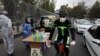 A biker wearing a face mask to curb the spread of the new coronavirus drives past a group of people selling hand sanitizer at a low price in Tajrish square in northern Tehran, April 16, 2020