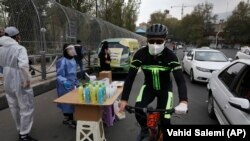 A biker wearing a face mask to curb the spread of the new coronavirus drives past a group of people selling hand sanitizer at a low price in Tajrish square in northern Tehran, April 16, 2020
