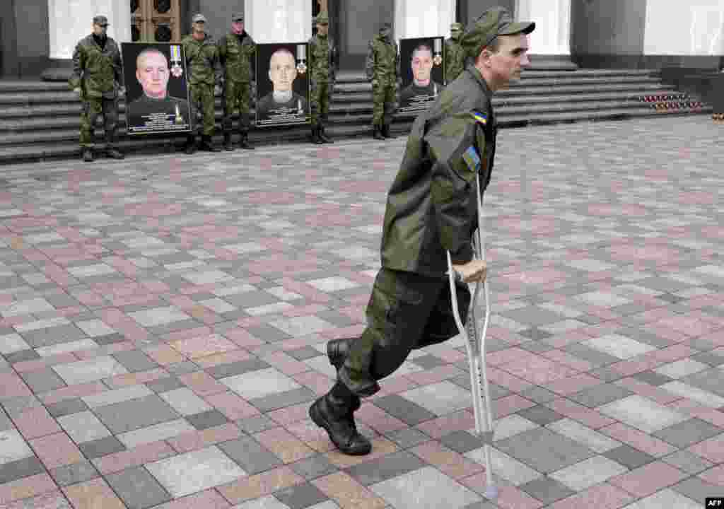 An injured serviceman of the National Guard of Ukraine walks in front of portraits of fallen comrades during a memorial service in front of the Ukrainian parliament in Kyiv. (AFP/Anatolii Stepanov)