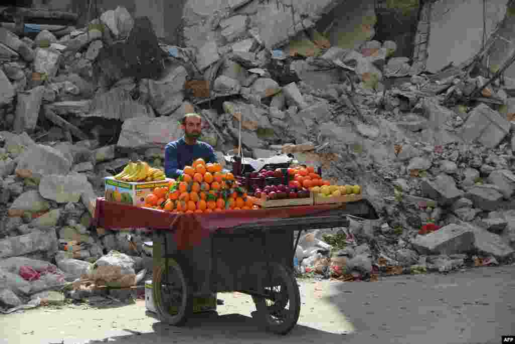 A fruit vendor waits for customers next to a damaged building in the Shaar neighborhood of the northern Syrian city of Aleppo. (AFP/Mohammed al-Khatieb)