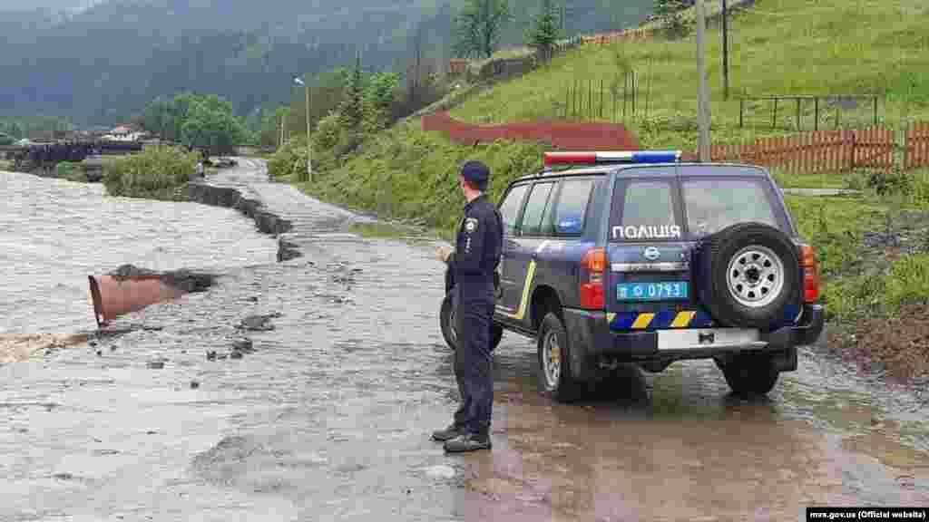 Un polițist supraveghează un drum distrus de inundații, pe 22 iunie.