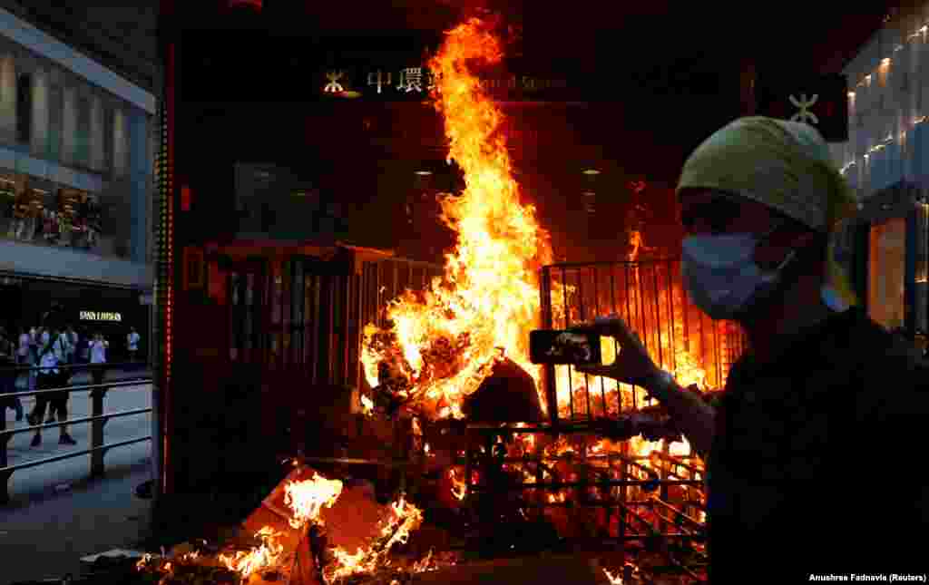 A protester films a fire at the entrance to MTR Central Station in Hong Kong. (Reuters/Anushree Fadnavis)