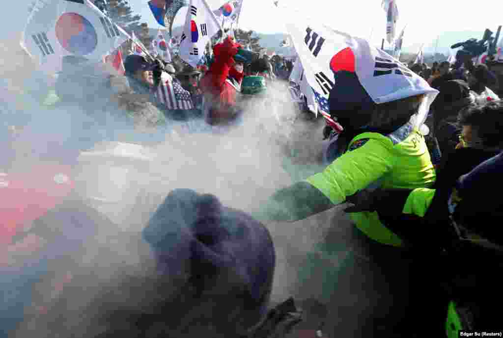 Поліція (у зеленому) зупиняє демонстрантів, які спалюють портрет північнокорейського лідера Кім Чен Ина під час акції протесту проти Північної Кореї перед церемонією відкриття зимової Олімпіади 2018 року в Пхьончхані&nbsp;