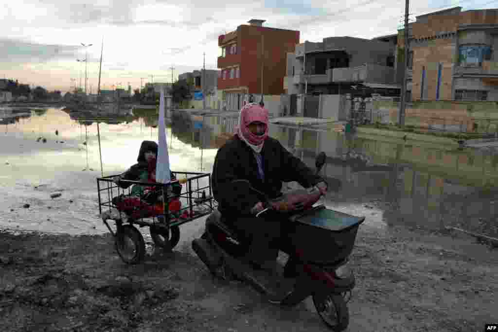 An Iraqi man drives a motorcycle, carrying a child and a white flag, in the Muharibin neighborhood of Mosul, as people gather for aid distribution. (AFP/Mahmud al-Samarrai)