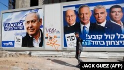 شهروندی از کنار پوسترهای نتانیاهو (چپ) و رقبایش می‌گذرد