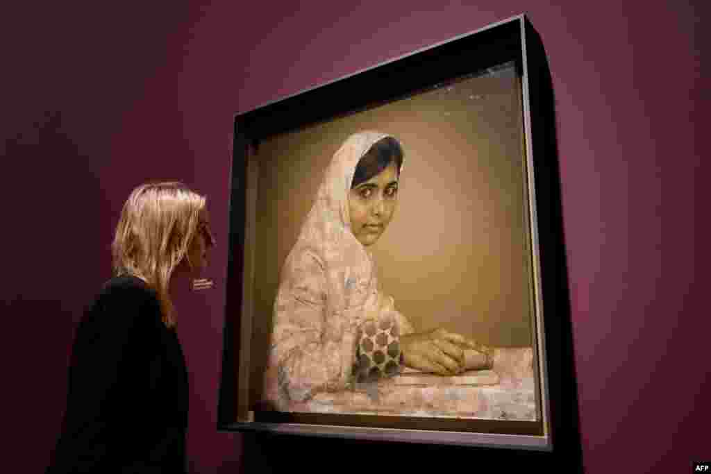 A worker at the National Portrait Gallery in London poses beside a portrait of Malala Yousafzai, the teenage Pakistani advocate for girls education who was shot in the head by the Taliban in 2012. (AFP/Leon Neal)