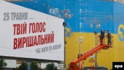 Сотрудники коммунальных служб на фоне плаката с надписью: "Твой голос - решающий". Киев, 21 мая 2014 года.