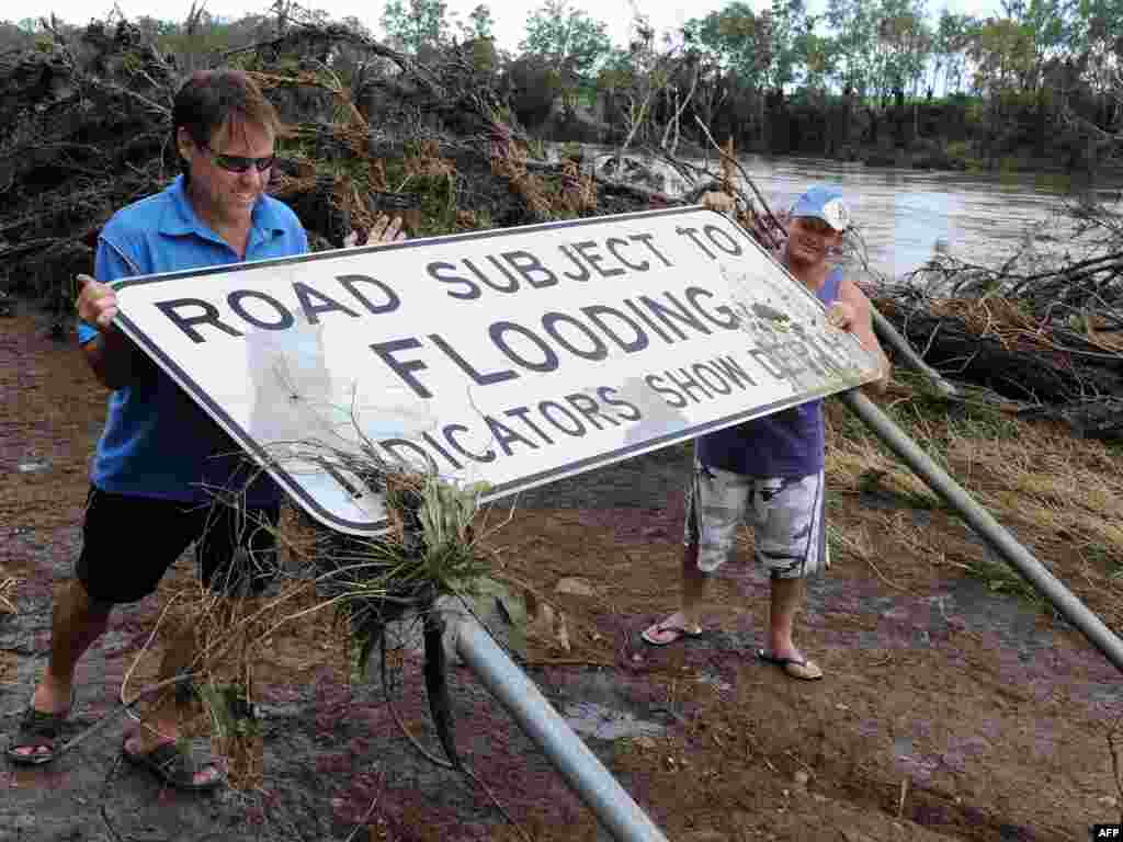 AUSTRALIA, Gin Gin : Residents Greg Messenger (L) and Gary Clem (R) try to restore a flood warning sign which had been flattened by the swollen Burnett River near the town of Gin Gin on January 2, 2011. Up to 200,000 people are estimated to have been hit by the floods which have left entire towns under water and cut off many more over an area the size of France and Germany combined, wreaking untold billions in damage to crops and the nation's key mining industry. AFP PHOTO / Torsten BLACKWOOD 