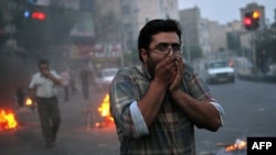 Protesters cover their faces from tear gas during clashes with riot police in Tehran on June 20