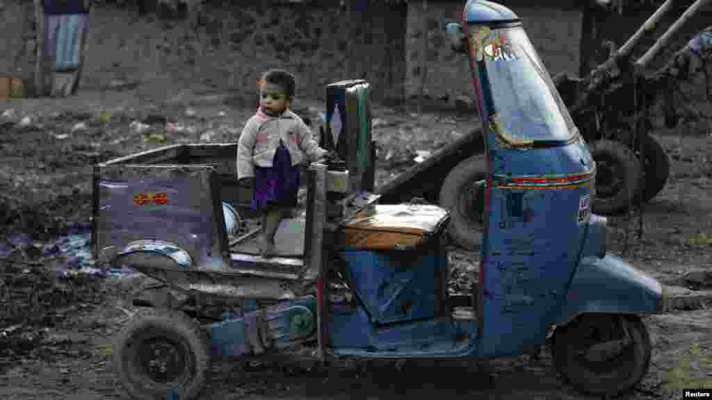 A child stands on the back of an auto rickshaw and watches as other children play in the outskirts of Islamabad. (REUTERS/Faisal Mahmood)