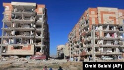 Survivors sit in front of government built housing units severely damaged by an earthquake, in Sarpol-e-Zahab, western Iran, November 13, 2017