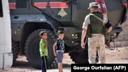 SYRIA -- Syrian children stand next to a member of the Russian military police in Jibrin, on the outskirts of Aleppo, August 16, 2017