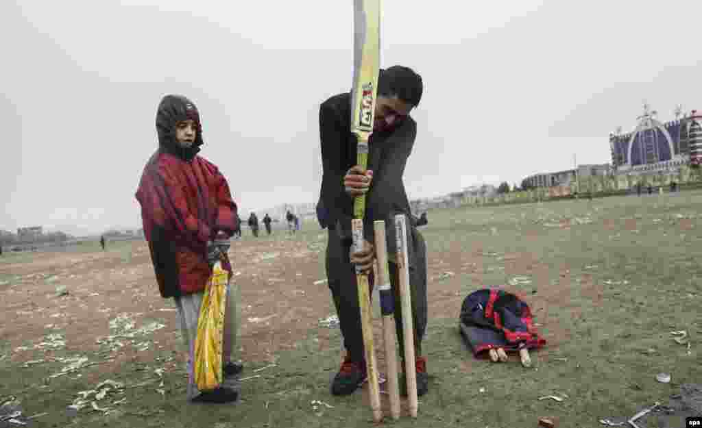 An older boy helps a younger player set up the wicket.