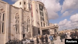 Residents of the northern Syrian city of Aleppo gather outside a building damaged in one of the bomb blasts there on February 10.