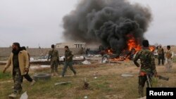 Shi'ite fighters known as Hashid Shaabi walk with their weapons as smoke rises from an explosives-laden military vehicle driven by an Islamic State suicide bomber, which exploded during an attack on the southern edge of Tikrit, on March 12.