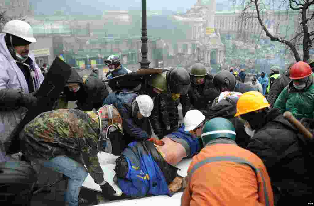 Antigovernment protesters carry away a wounded protester as riot policemen fire live bullets on them.