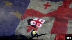 A man with a Georgian flag sits in front of a projection of the Georgian and European flags during celebrations for the signing of an Association Agreement with the European Union in Tbilisi on June 27.