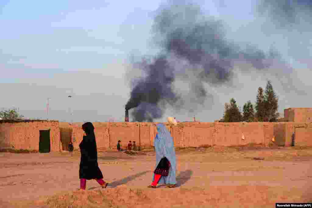 Afghan women walk near a brick factory as smoke rises from a chimney on the outskirts of Jalalabad. (AFP/Noorullah Shirzada)