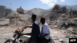 Men watch the demolition of a collapsed building in Port-au-Prince 